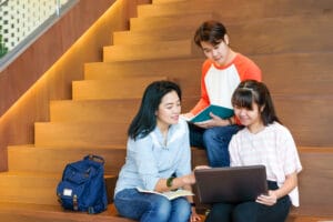 Group Asian Students Using Notebook Computer Tutoring Lesson With Their Lecturer While Sitting Library Stair Background